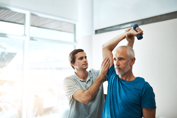 Ces exercices sont très importants pour votre rétablissement. Prise de vue d'un jeune physiothérapeute masculin aidant un client à faire des exercices d'étirement dans son bureau pendant la journée. - Photo, image