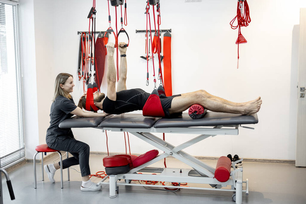 Rehabilitation specialist doing active treatment on suspension straps to a male patient - 写真・画像