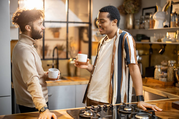 İki adam mutfakta konuşuyor ve kahve içiyor. - Fotoğraf, Görsel