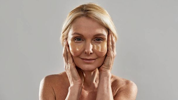 Mature woman touching face with under eye patches - Fotó, kép