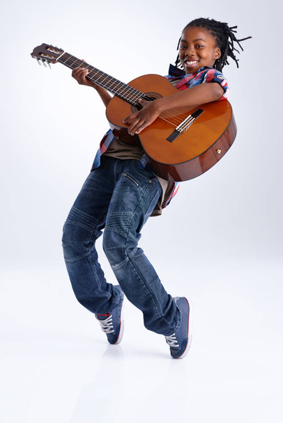 Κινήθηκε από τη μουσική. Ένα χαρούμενο νεαρό Αφροαμερικανό αγόρι που παίζει κιθάρα ενώ ισορροπεί στα δάχτυλα των ποδιών του.. - Φωτογραφία, εικόνα