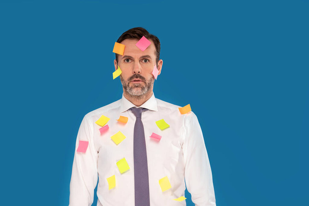 Tired male businessman in formal clothes posing over blue studio background, a lot of stickers on his body. Worker. Real people - Фото, изображение
