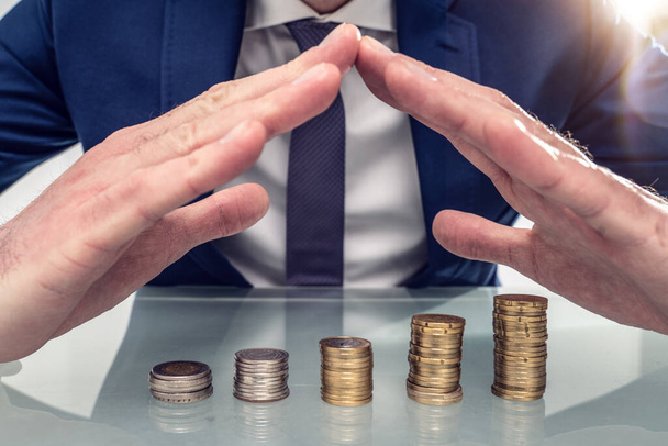 Close-up photo Of Businessperson Protecting Stack Of Coins With Hands At Desk - Photo, Image