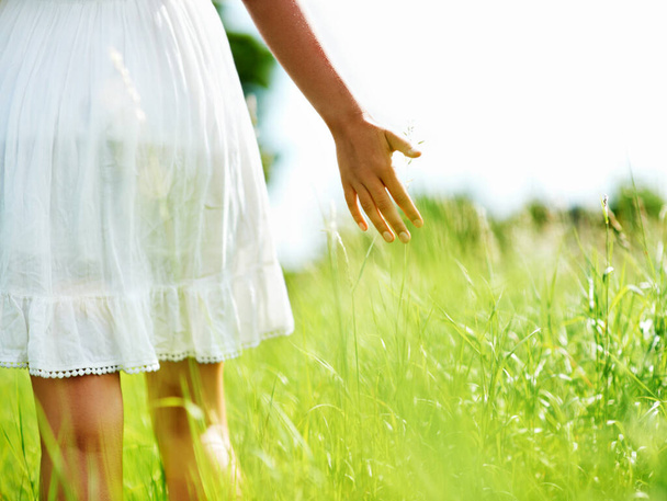 Tocando la naturaleza. Vista recortada de una joven caminando a través de un campo verde. - Foto, Imagen