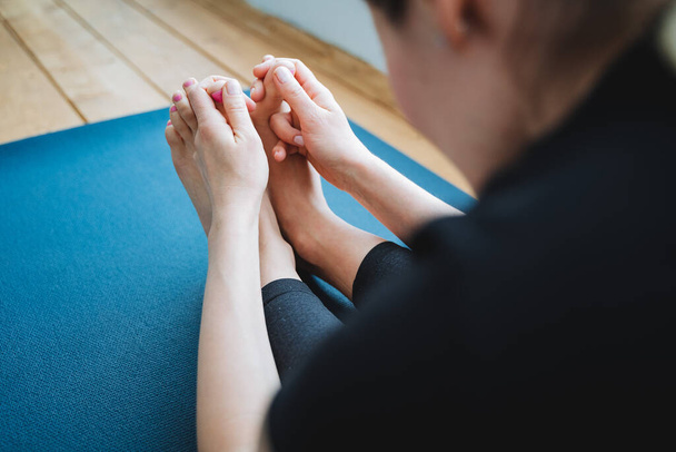 Hands with fingers hold feet Sedentary yoga pose with lean forward Capture of the big toe with your hand Stretching on a blue mat. High quality photo - Valokuva, kuva