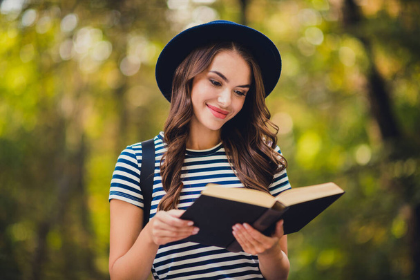 Portrait of attractive cheerful focused girl enjoying reading interesting book on fresh air outdoors - Foto, afbeelding
