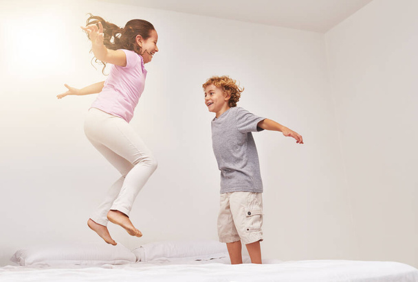 How high can you go. Shot of two little children jumping on a bed. - Фото, изображение