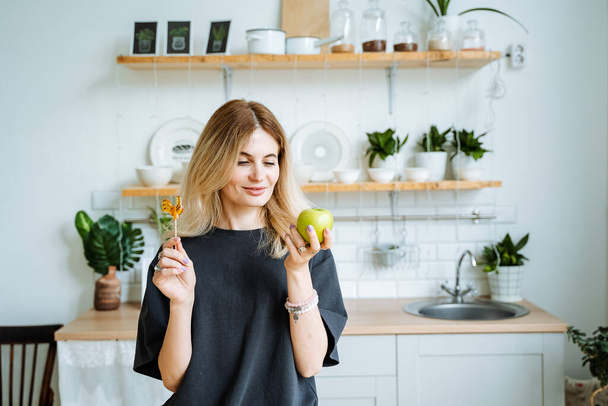 A girl in the kitchen holds an apple in her hands and wants to bite it off. Look at the apple. Healthy snack throughout the day, vegetarian food, fresh fruit. High quality photo - Foto, Imagen