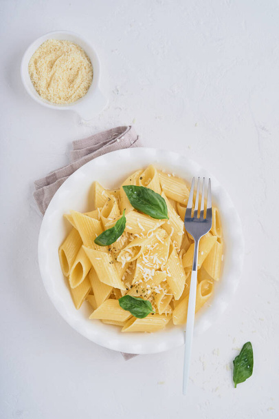 Tasty appetizing classic italian penne pasta with parmesan cheese and basil in white plate on plate on on stone table. Traditional dish of Italian cuisine. Top view. - Фото, изображение