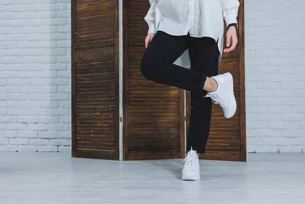 Close-up of female legs in black jeans in stylish leather white sneakers. Fashionable woman in new sneakers. Modern seasonal collection of stylish sneakers. Women's fashion. - Φωτογραφία, εικόνα