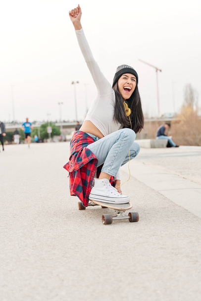 young latina enjoying herself while riding a skateboard. hispanic girl spending her leisure time doing outdoor sports. - 写真・画像
