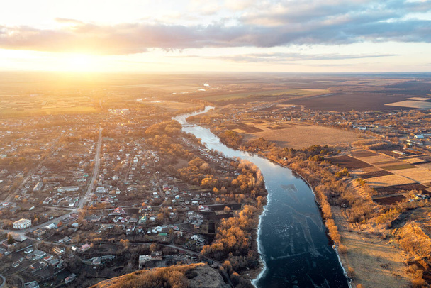 Θέα από ένα ύψος ενός γαλάζιου ποταμού περιέλιξης που εκτείνεται σε απόσταση. Φθινόπωρο τοπίο στο ηλιοβασίλεμα - Φωτογραφία, εικόνα