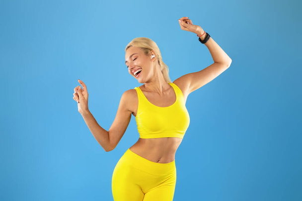Усміхнена молода жінка в спортивному одязі слухає музику і танцює
 - Фото, зображення