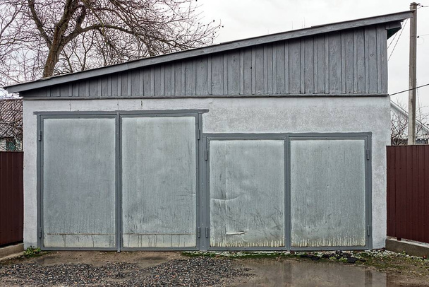 fachada de un garaje rural con dos puertas de metal gris en la calle - Foto, Imagen