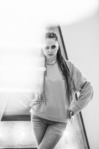 Portrait of a young girl in jeans and a sweatshirt with bright makeup on her face. Girl with afro braids. Defocusing, selective focus. Black and white photo. - Foto, Bild