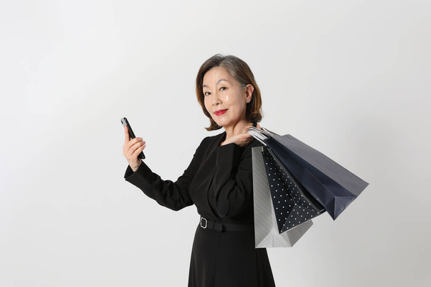 fashionable Asian Korean senior woman, holding a smartphone and shopping bag - Foto, immagini