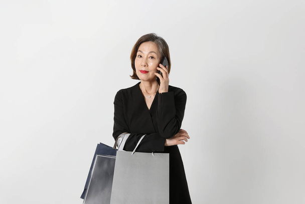 fashionable Asian Korean senior woman, holding a shopping bag calling on phone - Фото, зображення