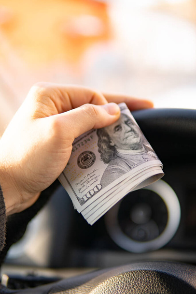 Closeup holding dollar bills in car dealership background. Personal transportation purchase concept - Photo, Image