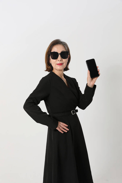fashionable Asian Korean senior woman, wearing sunglasses and holding a smartphone - Foto, afbeelding