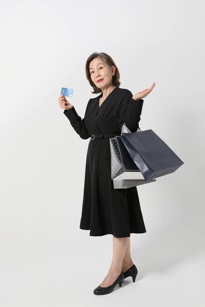 fashionable Asian Korean senior woman, holding a credit card and shopping bag - Foto, afbeelding