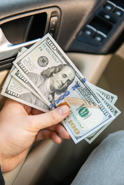A dollar bills in the male hand on the background of the steering wheel in the car. Concept of earnings or bribes, insurance or credit - Photo, Image
