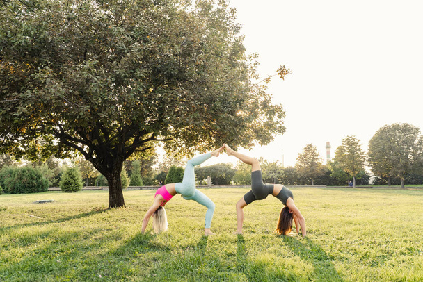 Joga i gimnastyka trening sportowy 2 dziewczyny na zewnątrz w parku o zachodzie słońca. Styl życia sportu - Zdjęcie, obraz