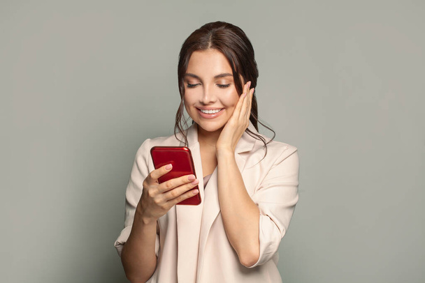 Überraschte Frau mit Smartphone lächelt glücklich und hält Hand in Wange - Foto, Bild