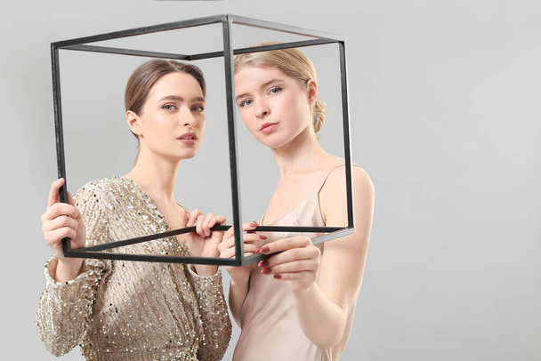 Portrait of stylish young sisters with frame on light background - Fotografie, Obrázek