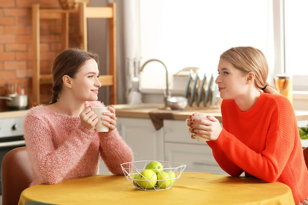 Young sisters drinking tea in kitchen at home - Foto, imagen