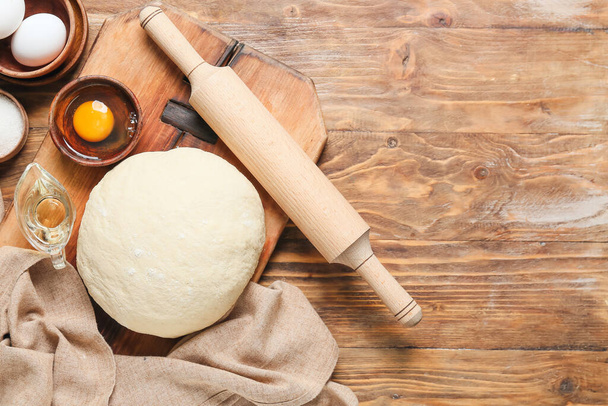 Raw dough with rolling pin and ingredients on wooden background - Photo, Image
