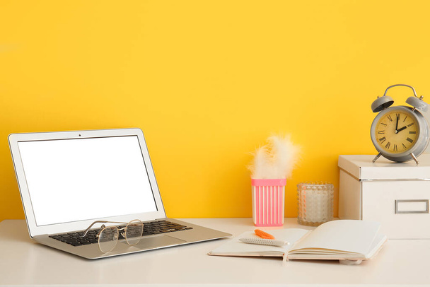 Modern laptop, szemüveg és írószer kellékek az asztalon közel színes fal - Fotó, kép