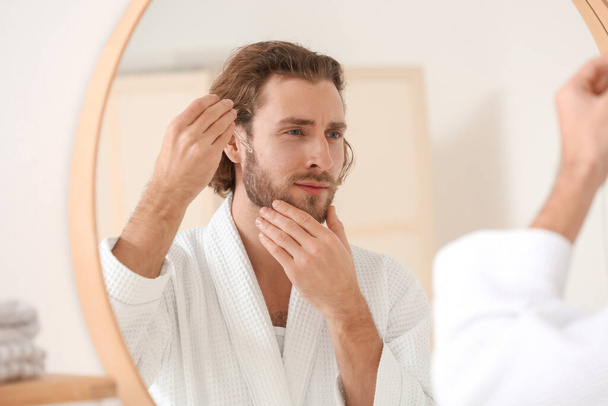 Young man using serum for skin care in bathroom - Foto, imagen