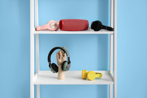 Unidad de estante con altavoz portátil inalámbrico y diferentes auriculares cerca de la pared de color - Foto, imagen