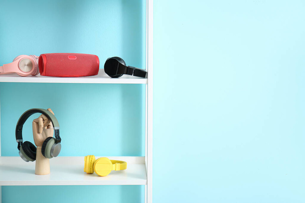 Shelf unit with wireless portable speaker and different headphones near color wall - Φωτογραφία, εικόνα