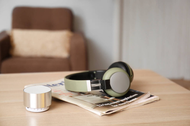 Vezeték nélküli hordozható hangszóró, modern fejhallgató és magazin fából készült asztalon a szobában - Fotó, kép