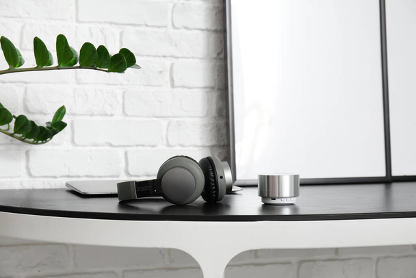 Ασύρματο φορητό ηχείο και ακουστικά στο τραπέζι κοντά στο λευκό τοίχο τούβλο - Φωτογραφία, εικόνα