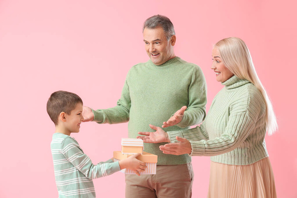 Menino dando presentes para seus avós em camisolas quentes no fundo rosa - Foto, Imagem