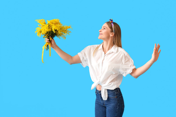 Гарна жінка з квітами мімози на синьому тлі. Міжнародний жіночий день - Фото, зображення