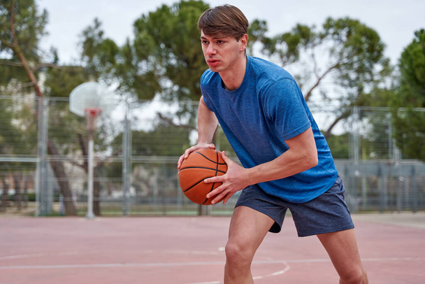 joven atleta entrena al aire libre. hombre caucásico jugando baloncesto en una cancha, practicando driblar con la pelota. - Foto, imagen