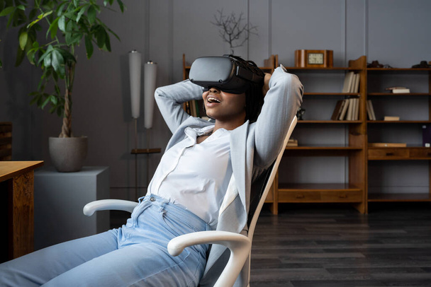 Donna d'affari nera stupita che utilizza VR sul posto di lavoro, riposandosi in un rilassante ambiente virtuale in ufficio - Foto, immagini