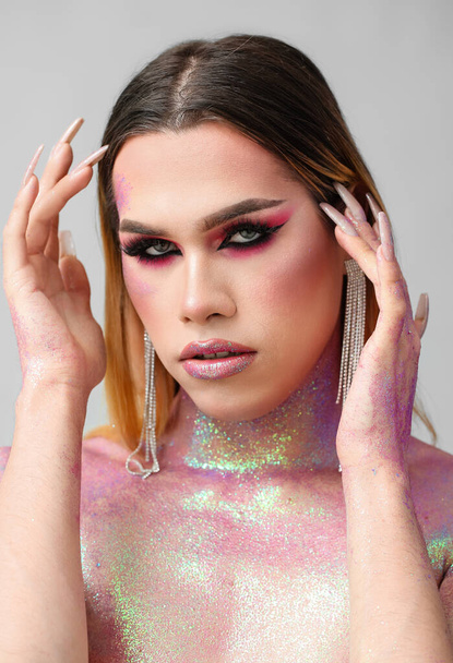 Modieuze jonge transgender vrouw met glitters op het lichaam tegen lichte achtergrond - Foto, afbeelding