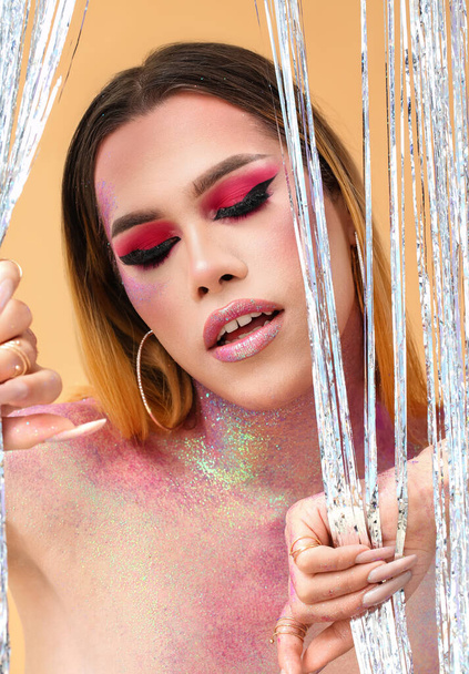 Alla moda giovane donna transgender con brillantini sul corpo contro lo sfondo di colore - Foto, immagini
