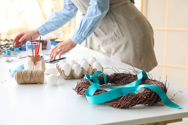 Couronne de Pâques avec ruban, oeufs, corde à ficelle et verre avec brosses sur la table - Photo, image