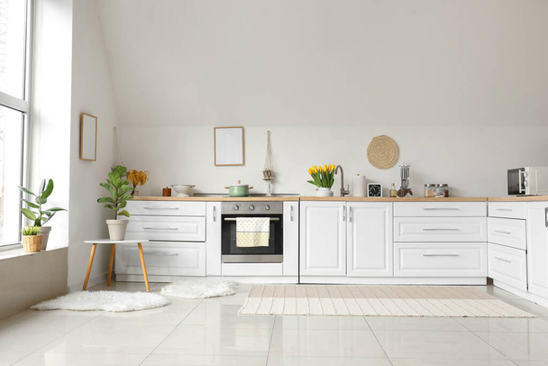 Кухонные прилавки с посудой и красивыми цветами возле белой стены в интерьере комнаты - Фото, изображение