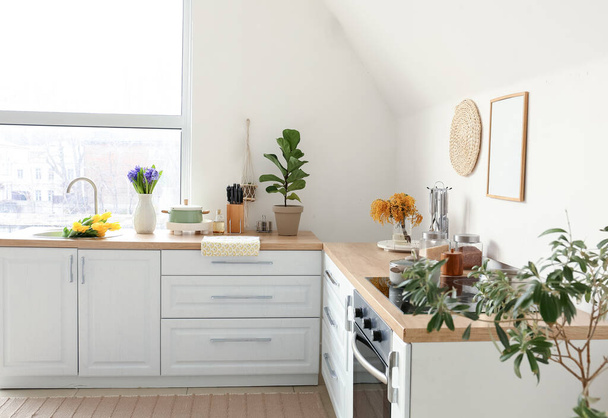 白い壁の近くに美しい花や道具とキッチンカウンター - 写真・画像