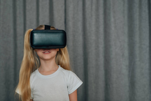 κορίτσι παιδί στο σπίτι σε εικονική πραγματικότητα γυαλιά VR βλέποντας βίντεο, παίζοντας παιχνίδια. Τα σύγχρονα παιδιά γνωρίζουν καλά τις τεχνολογικές καινοτομίες. γενεά άλφα. Υψηλής ποιότητας φωτογραφία - Φωτογραφία, εικόνα