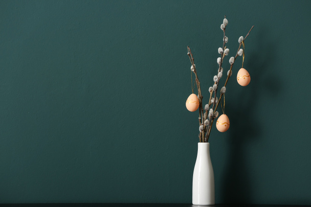 Vase with pussy willow branches and painted Easter eggs on table near green wall - Foto, immagini