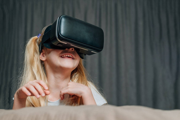 Evde sanal gerçeklik gözlüklü çocuk video izleyip oyun oynuyor. Modern çocuklar teknolojik yenilikler konusunda çok bilgilidirler. Alfa kuşağı. Yüksek kalite fotoğraf - Fotoğraf, Görsel