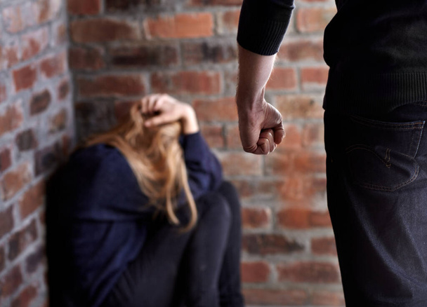 Tratando de esconderme. Mujer joven maltratada con las manos en el pelo mientras su abusador se para frente a ella. - Foto, Imagen