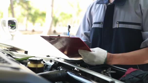 Los mecánicos profesionales inspeccionan las camionetas de los clientes en el garaje, usan portapapeles para escribir registros de mantenimiento, verificar el estado del motor y el equipo que deben reemplazarse. - Metraje, vídeo